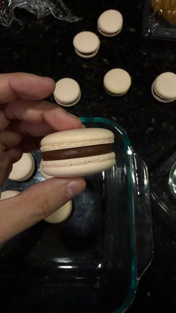 Macaron rosado relleno de ganache de chocolate sostenido en la mano