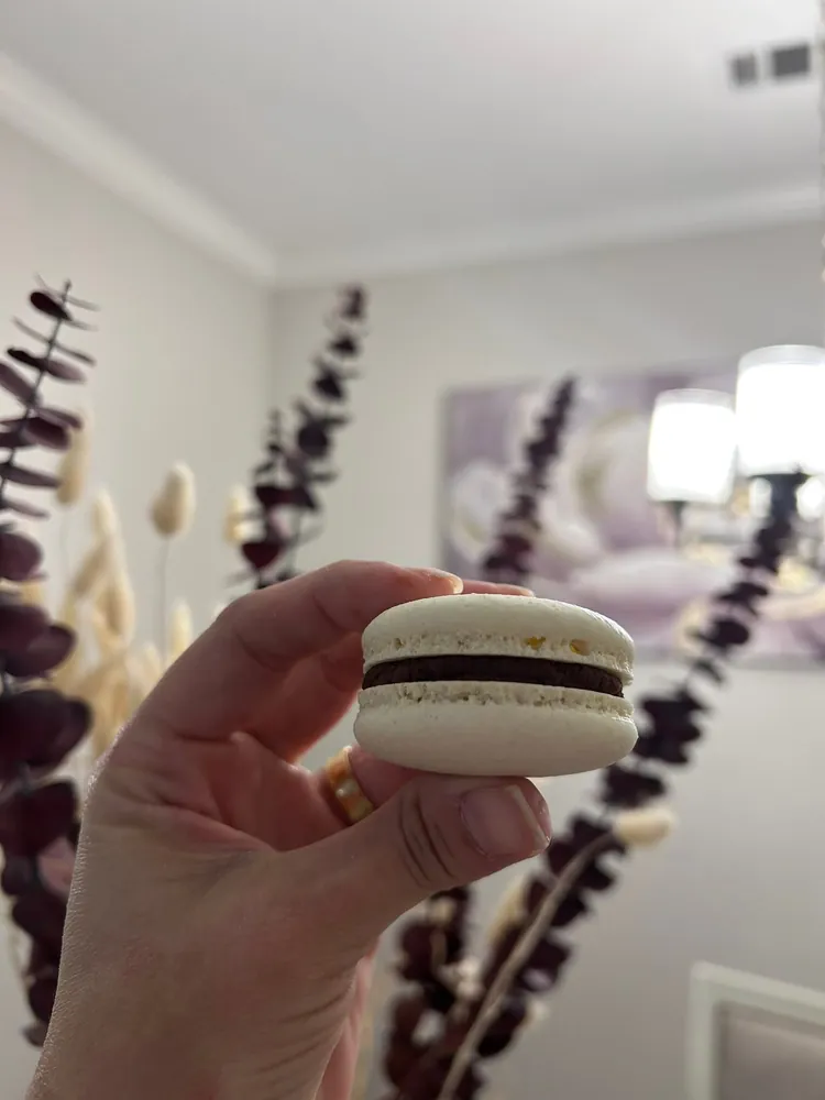 Macaron de vainilla relleno de ganache de chocolate sostenido en la mano