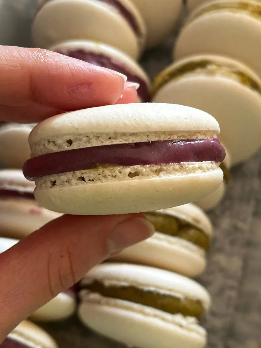 Macaron relleno de ganache de frutos rojos sostenido entre los dedos
