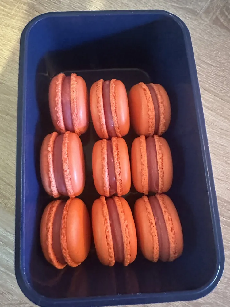 Nueve macarons naranja rellenos en un recipiente azul