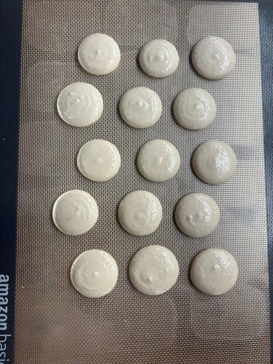 Tapas de macaron recién dosificadas con un pico en el centro que no se asentó