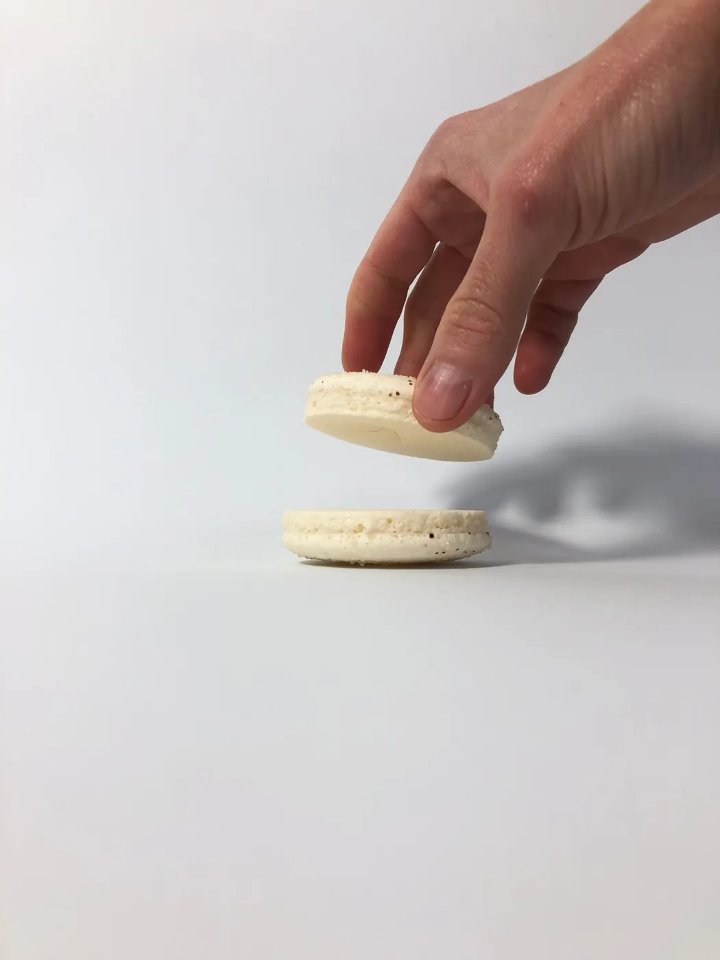 Mano colocando la tapa superior de un macaron de vainilla durante el armado