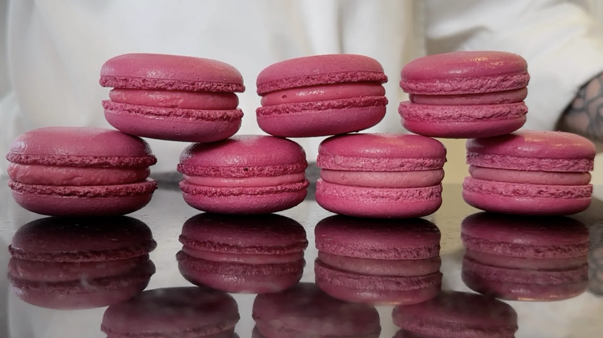 Siete macarons de frambuesa con pie parejo sobre una superficie espejada