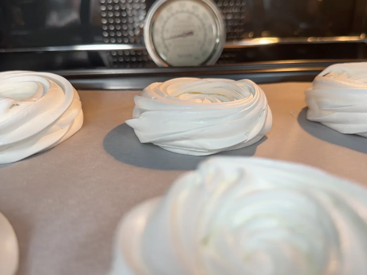 Nidos de merengue horneándose, con un termómetro de horno al fondo