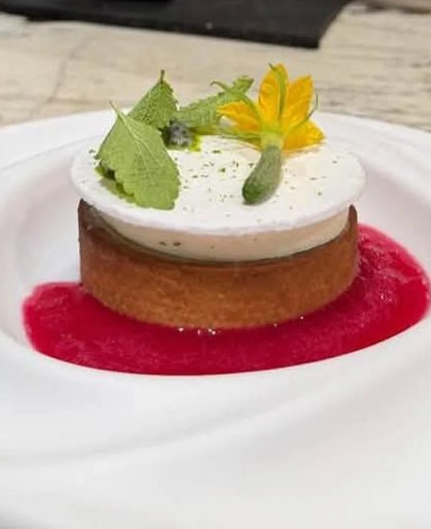 Tartaleta emplatada sobre salsa roja, con flor de calabacín y hojas