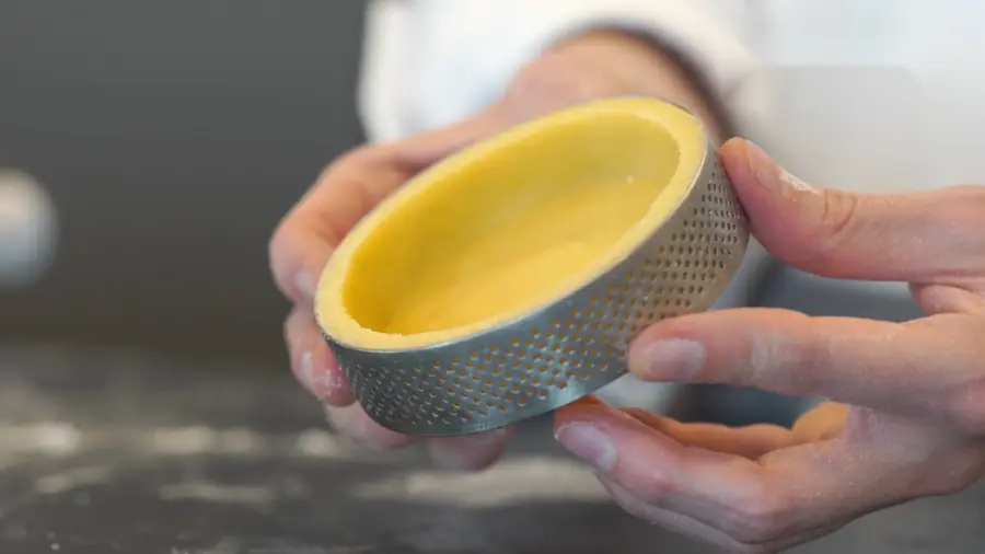 Manos sostienen un aro perforado con la masa ya fonzada