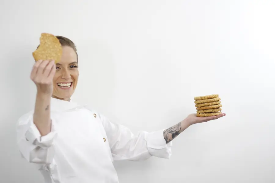 Moni Ríos sonríe con una galleta en una mano y una torre de cookies en la otra