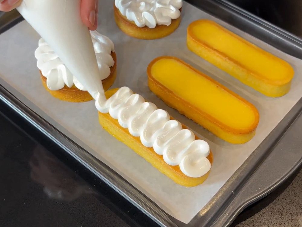 Tartaletas de limón recibiendo el merengue con manga pastelera